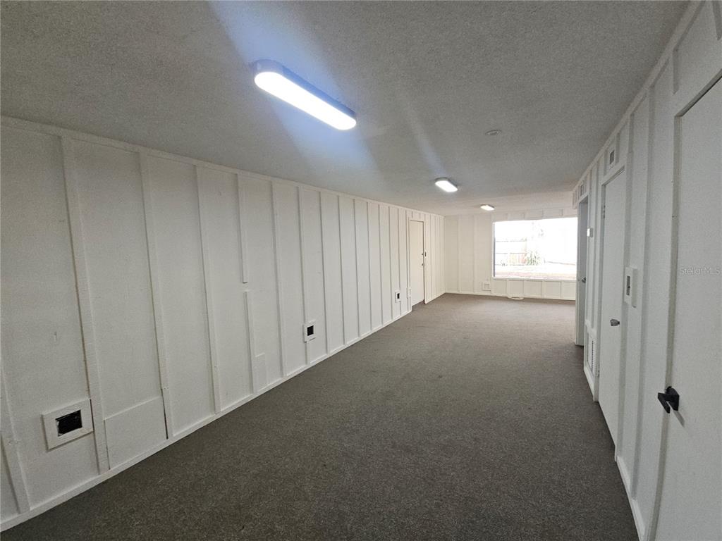 A long, narrow room features white vertical-paneled walls, gray carpeting, and multiple ceiling lights — 529 N FERN CREEK AVENUE, ORLANDO, FL