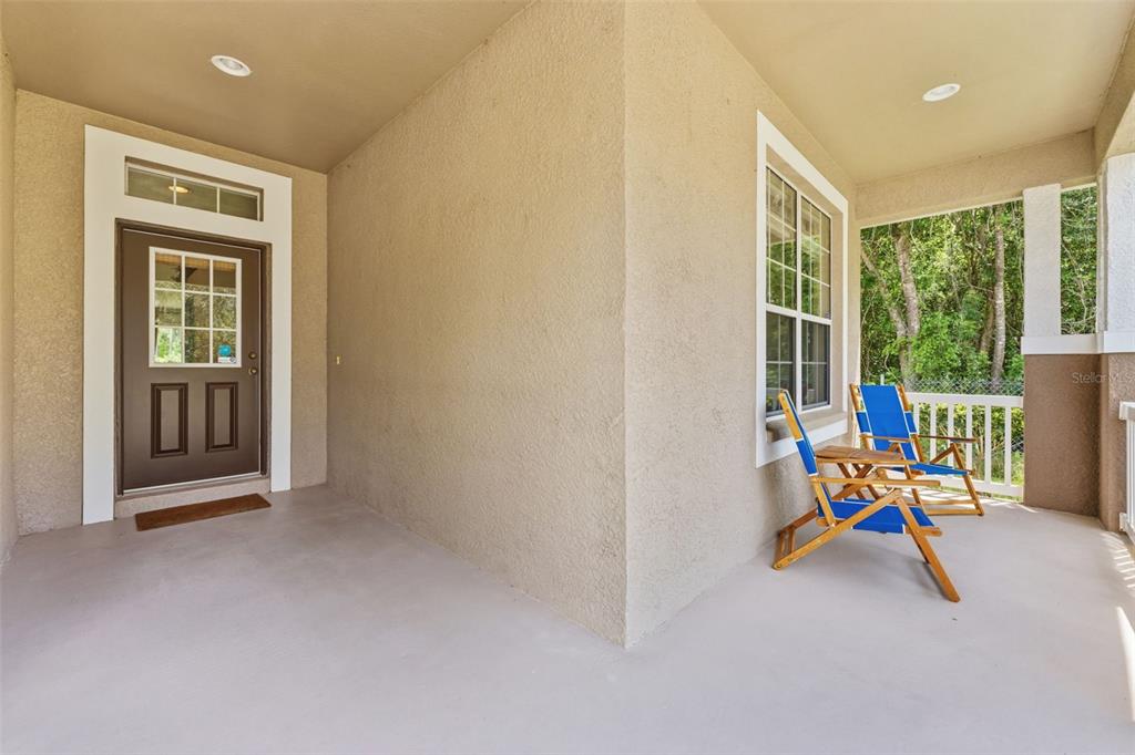 A covered front porch features a brown door, beige stucco walls, and two blue chairs — 5154 PHEASANT WOODS DRIVE, LUTZ, FL