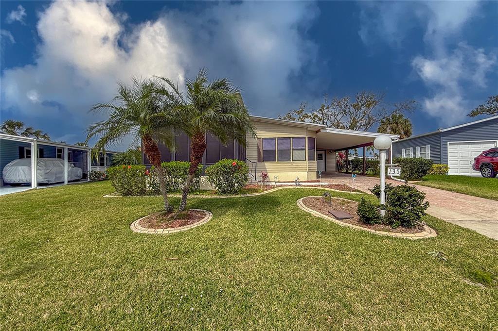 A single-story manufactured home with a palm tree, carport, and landscaped lawn — 135 HUMMINGBIRD AVENUE, ELLENTON, FL