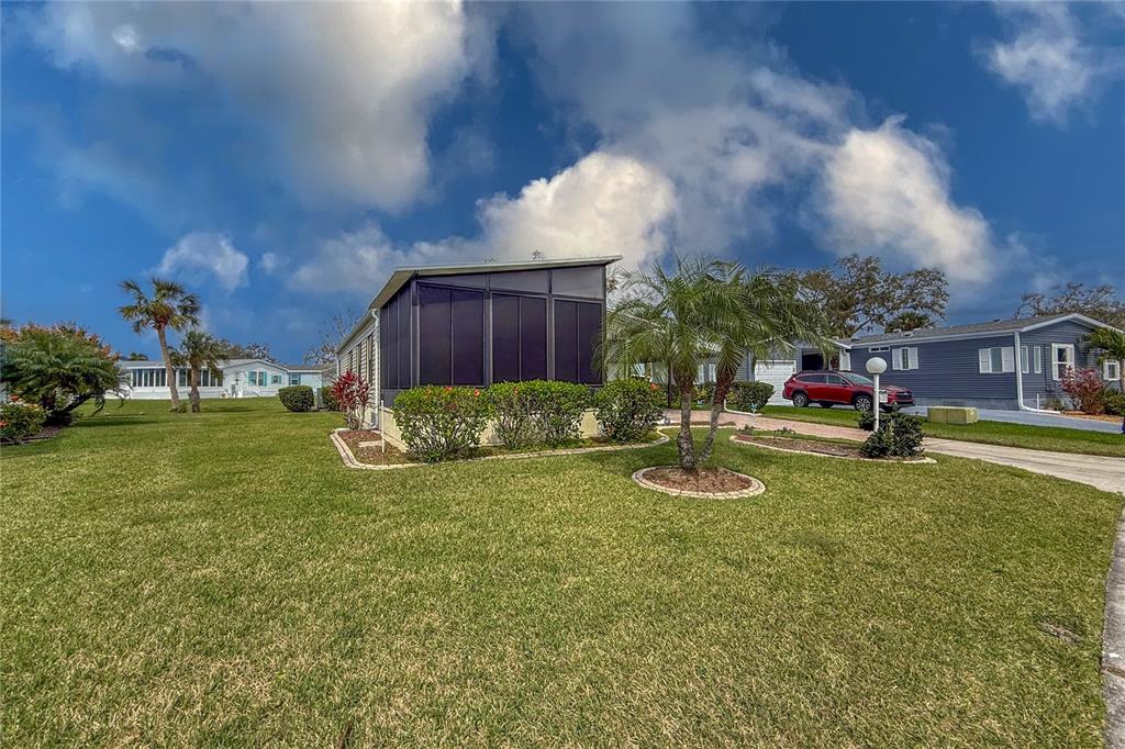 A mobile home with a screened-in porch sits on a grassy lot with palm trees — 135 HUMMINGBIRD AVENUE, ELLENTON, FL