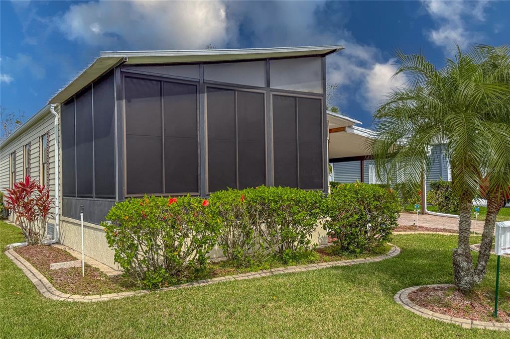 A screened-in porch with a sloped roof sits beside a palm tree and landscaped bushes — 135 HUMMINGBIRD AVENUE, ELLENTON, FL