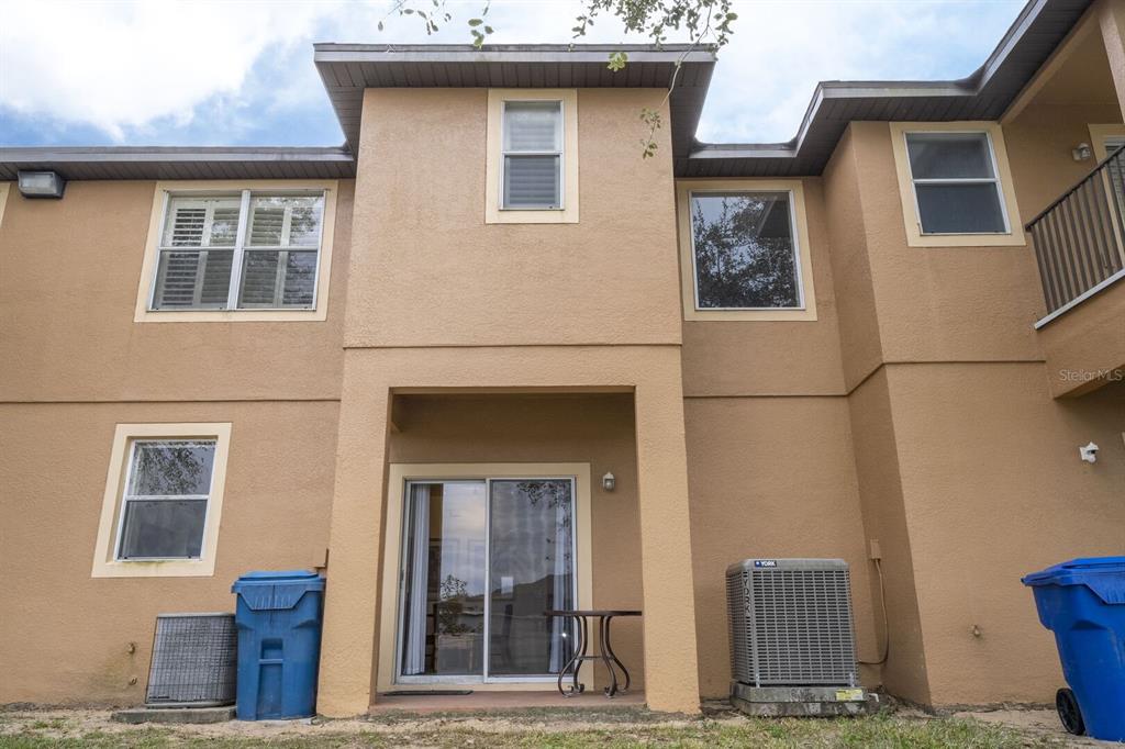 The exterior of a two-story tan stucco building features a patio with sliding glass doors — 3132 CALABRIA AVENUE, DAVENPORT, FL
