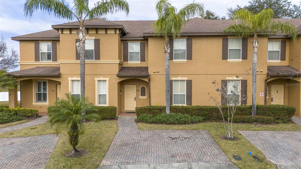A two-story tan townhouse with brown shutters, a brick walkway, and two palm trees — 3132 CALABRIA AVENUE, DAVENPORT, FL