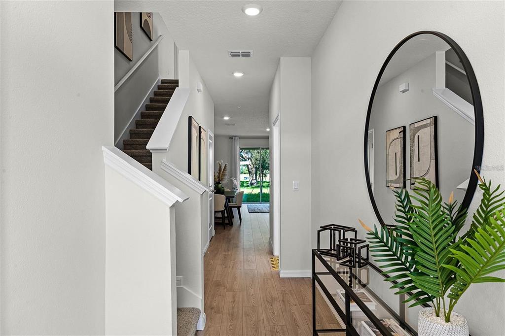 A bright entryway features wood-look flooring, a staircase with carpeted steps, and a round mirror — 14385 CANVAS STREET, ORLANDO, FL