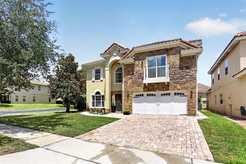 A two-story house with a stone facade, white garage doors, and a brick paver driveway — 7035 BRESCIA WAY, ORLANDO, FL