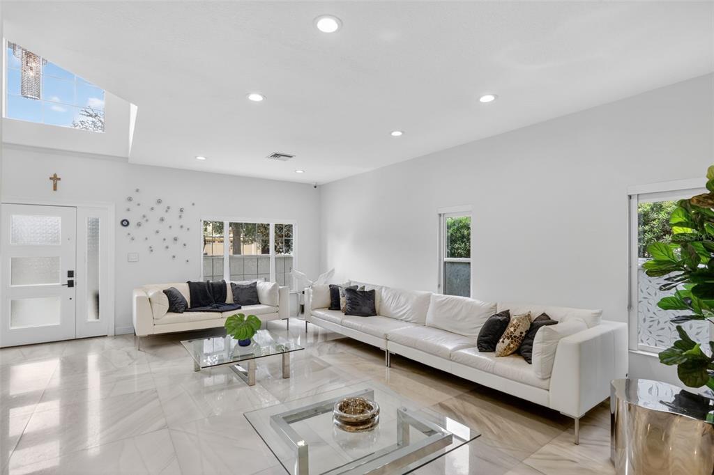 A bright living room features white leather sofas, glass coffee tables, and marble-look tile flooring — 7035 BRESCIA WAY, ORLANDO, FL