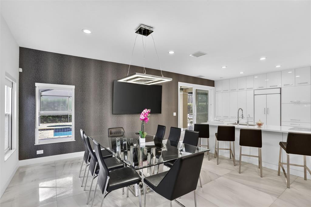 A modern dining area with a glass table, black chairs, and white kitchen cabinetry — 7035 BRESCIA WAY, ORLANDO, FL