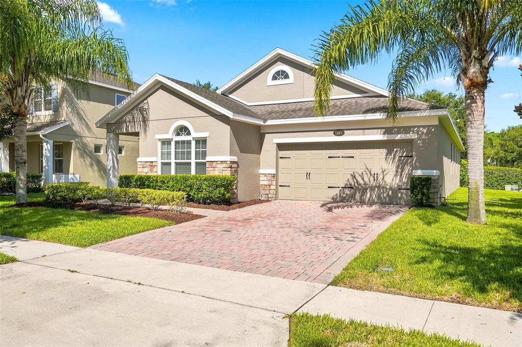 A single-story suburban house with a tan stucco exterior, stone accents, and a brick driveway — 1061 COSMOS WAY, OVIEDO, FL
