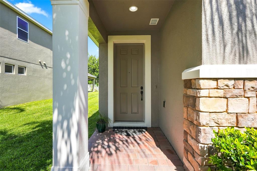 A front entryway features a brown door, a stone pillar, and a paved porch — 1061 COSMOS WAY, OVIEDO, FL