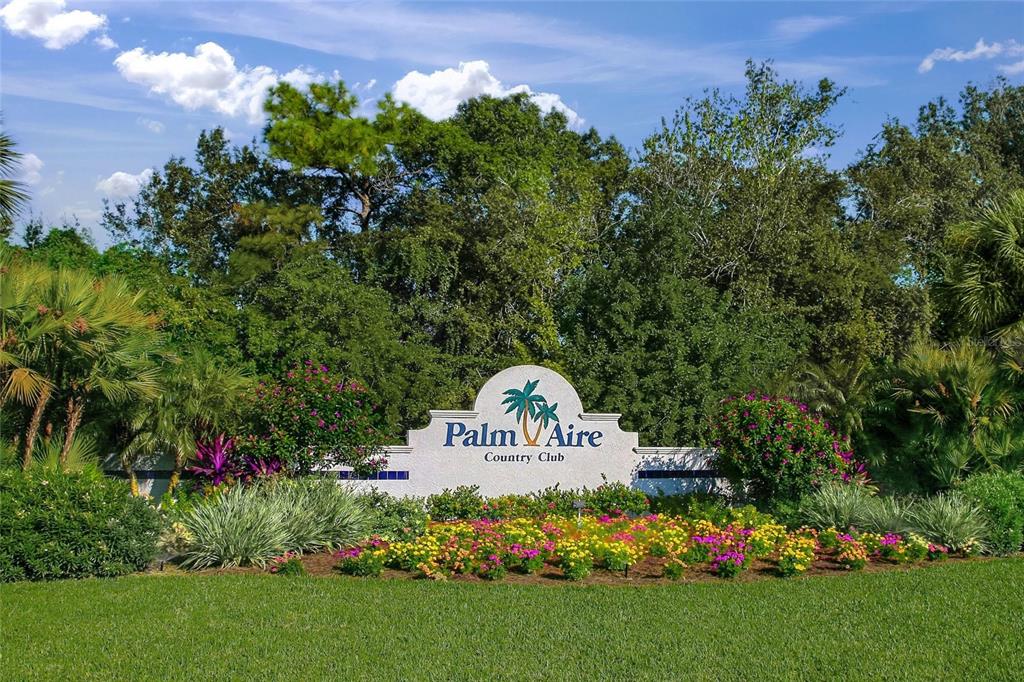 A white monument sign for Palm Aire Country Club sits in front of lush landscaping — 7860 PALM AIRE LANE UNIT 105, SARASOTA, FL