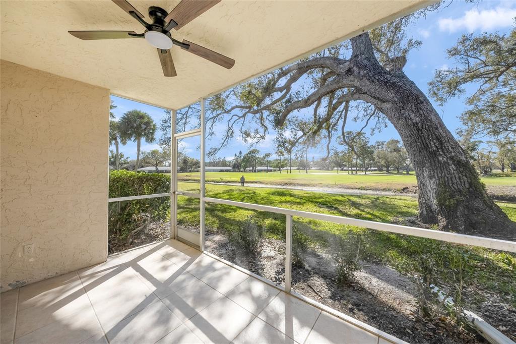 A screened-in patio with tile flooring overlooks a grassy golf course and a large tree — 7860 PALM AIRE LANE UNIT 105, SARASOTA, FL