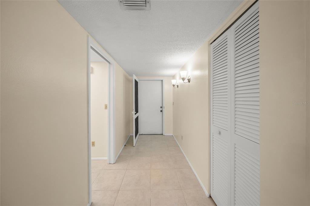 A hallway with beige tile flooring, light walls, a white door, and louvered closet doors — 7860 PALM AIRE LANE UNIT 105, SARASOTA, FL