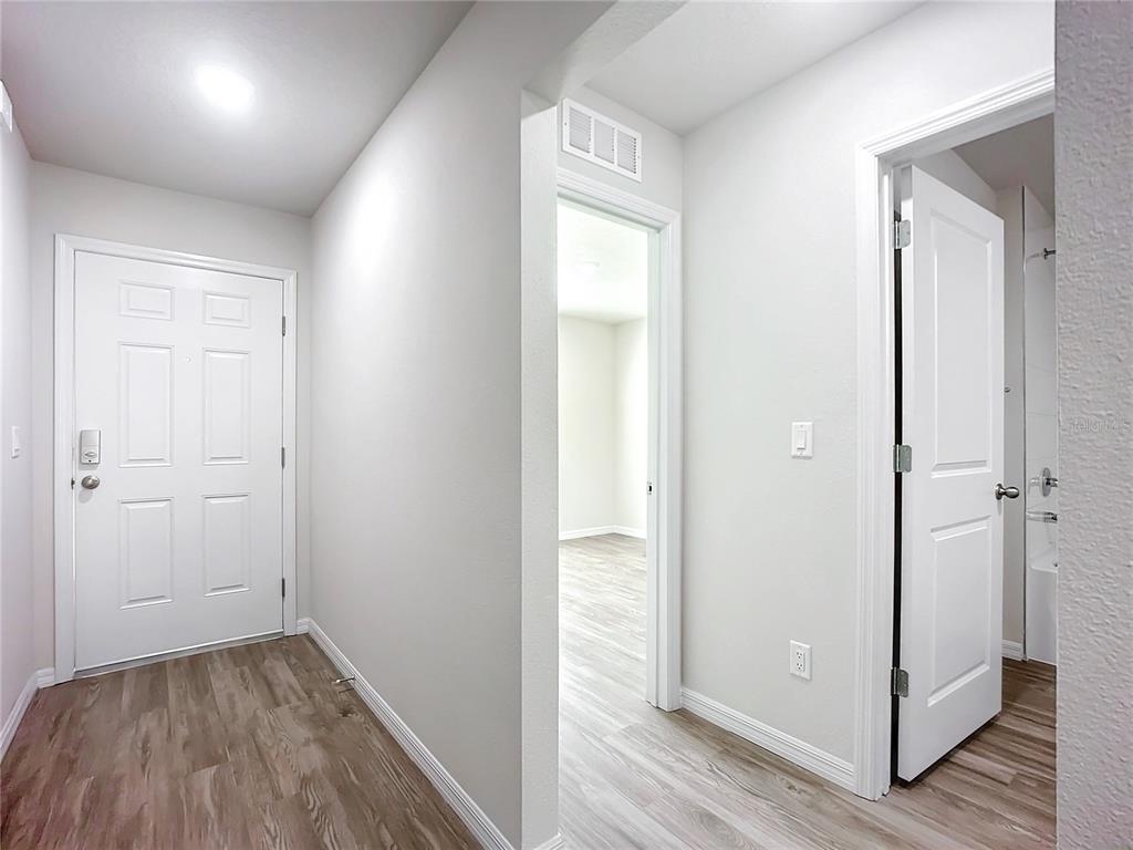 A hallway with light wood-look flooring leads to an open doorway and a closed door — 13 UNIQUE COURT, PALM COAST, FL