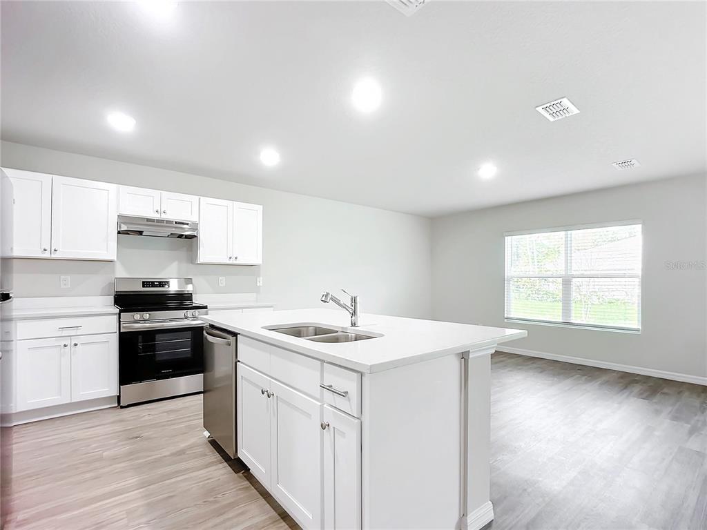 A modern kitchen features white cabinets, a central island with a sink, and stainless appliances — 13 UNIQUE COURT, PALM COAST, FL