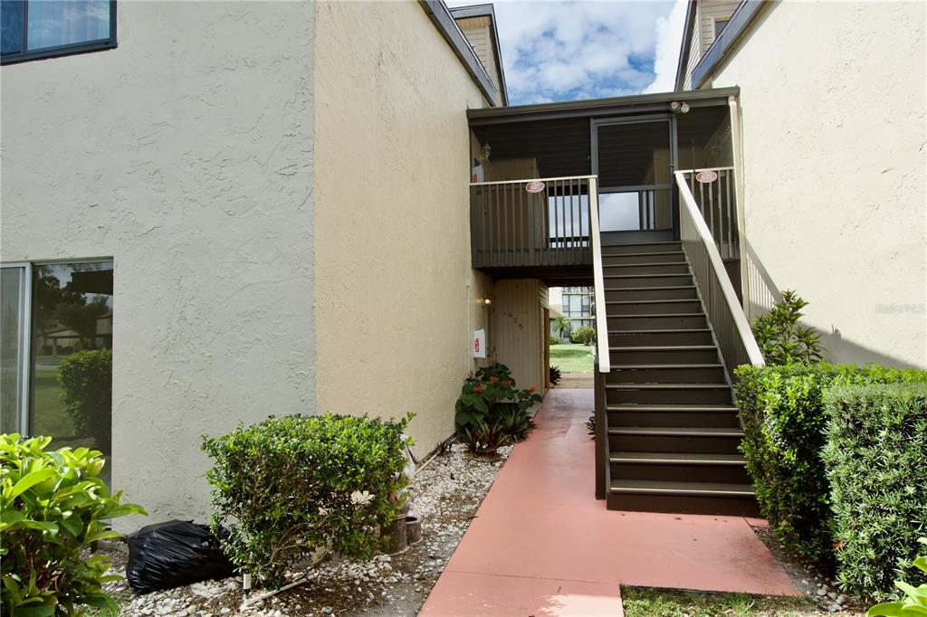 An exterior view of a multi-story building with a wooden staircase leading to a balcony — 625 WHITE PINE TREE ROAD UNIT 23, VENICE, FL