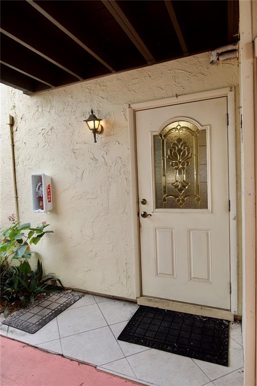 A white front door with a decorative glass insert sits on a tiled porch — 625 WHITE PINE TREE ROAD UNIT 23, VENICE, FL
