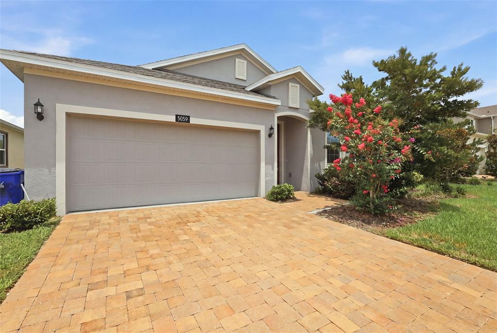 A single-story house with a beige stucco exterior, a paved driveway, and a flowering tree — 5059 TIBET COURT, ST CLOUD, FL