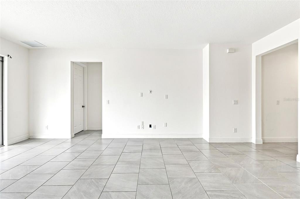 A bright, empty living room features white walls, gray tile flooring, and multiple wall outlets — 5059 TIBET COURT, ST CLOUD, FL