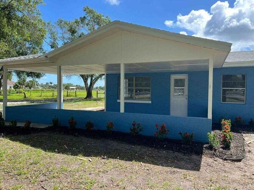 A blue house exterior features a covered porch with white posts and a white door — 2410 S Brocksmith Road, Fort Pierce FL 34945, FORT PIERCE, FL