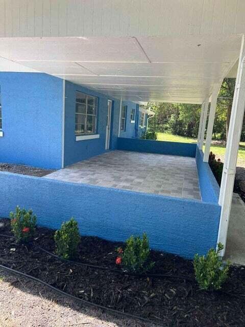 A covered patio with light-colored pavers and a blue stucco wall sits beside a house — 2410 S Brocksmith Road, Fort Pierce FL 34945, FORT PIERCE, FL