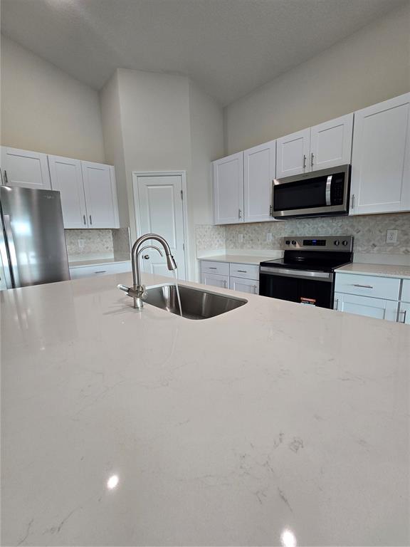 A kitchen features white cabinets, stainless steel appliances, and a large quartz-topped island — 1728 VANILLA STREET, HAINES CITY, FL