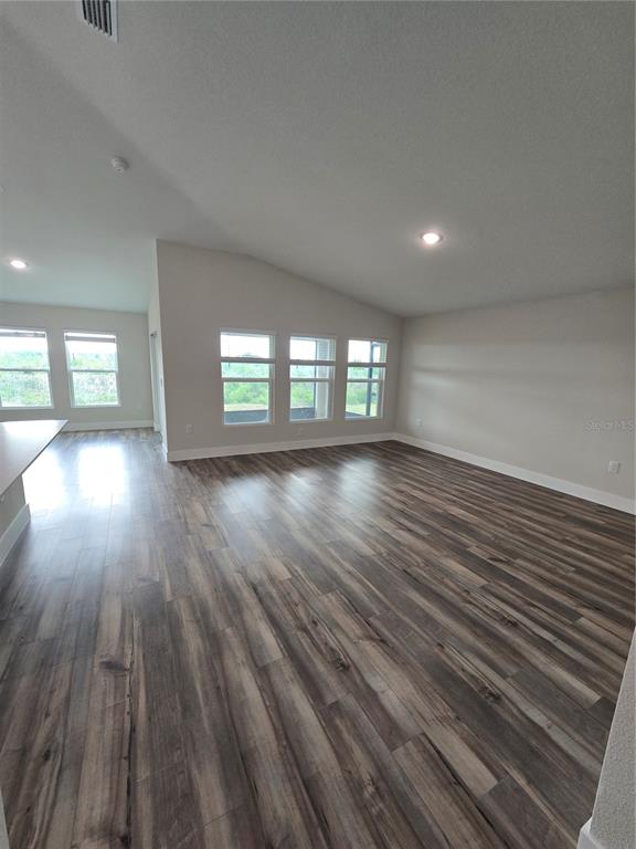 An open-concept living area features wood-look flooring, vaulted ceilings, and large windows — 1728 VANILLA STREET, HAINES CITY, FL