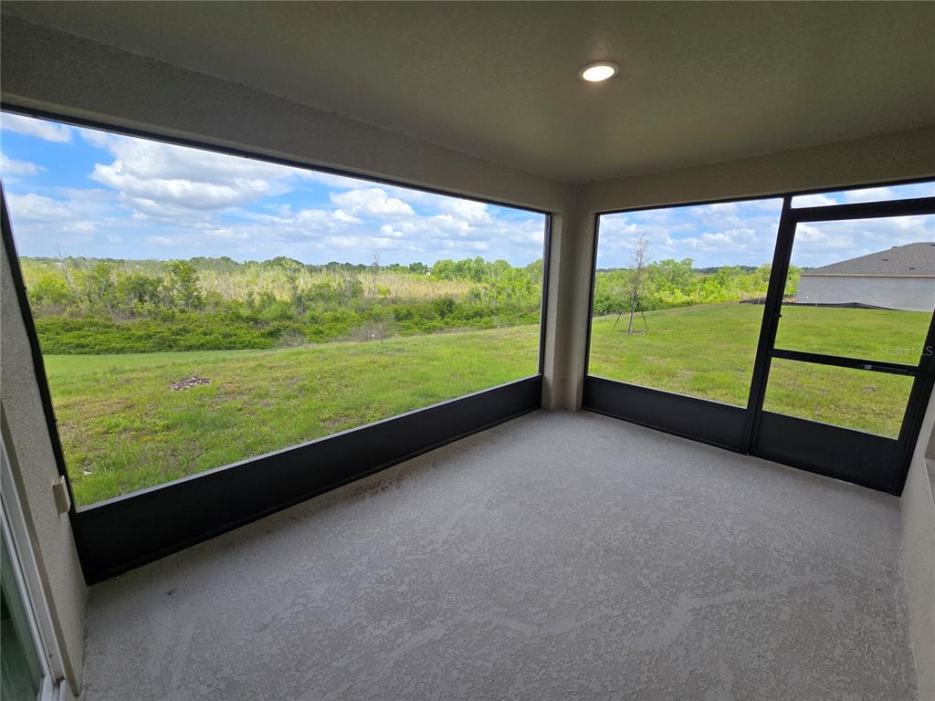 A screened-in porch with a concrete floor overlooks a grassy yard and distant trees — 1728 VANILLA STREET, HAINES CITY, FL
