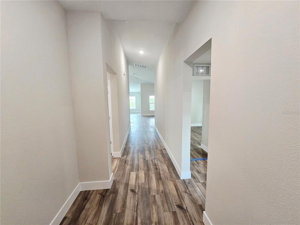 A hallway with light-colored walls and wood-look flooring leads toward a bright living area — 1728 VANILLA STREET, HAINES CITY, FL