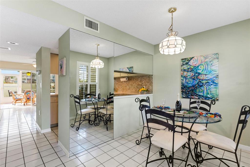 A dining area with a glass table, wrought iron chairs, mirrored wall, and tile flooring — 744 CADIZ ROAD UNIT 7, VENICE, FL