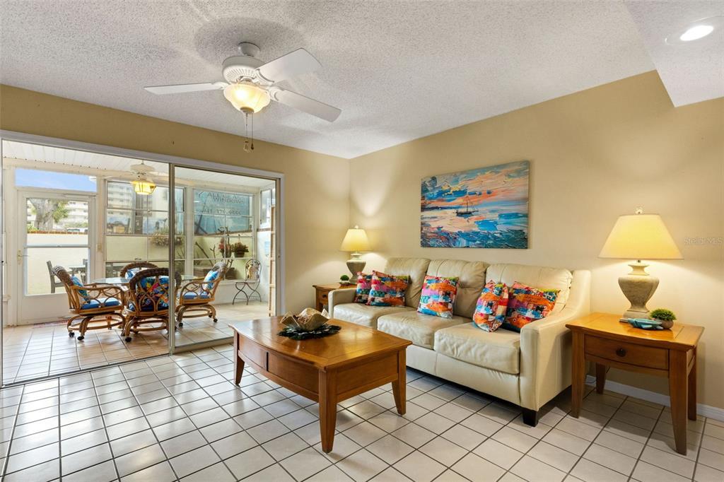 A living room with a beige sofa, wooden coffee table, tile floors, and a sliding door — 744 CADIZ ROAD UNIT 7, VENICE, FL
