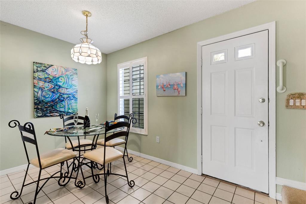 A dining area features a glass-top table, tile flooring, light green walls, and a white door — 744 CADIZ ROAD UNIT 7, VENICE, FL