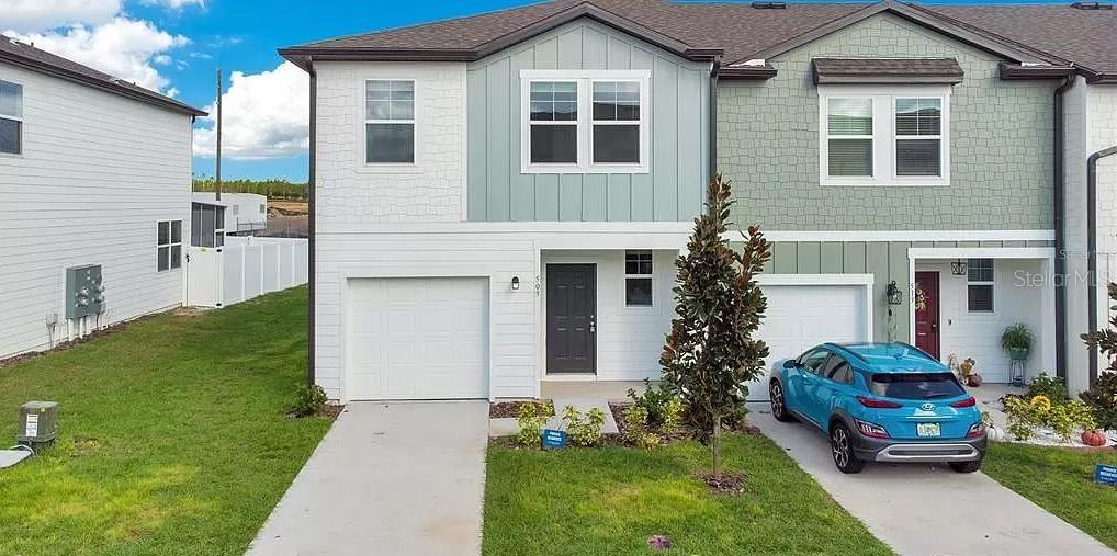The exterior of two adjacent townhomes features white, light green, and textured siding with garages — 509 MADISON DRIVE, DAVENPORT, FL