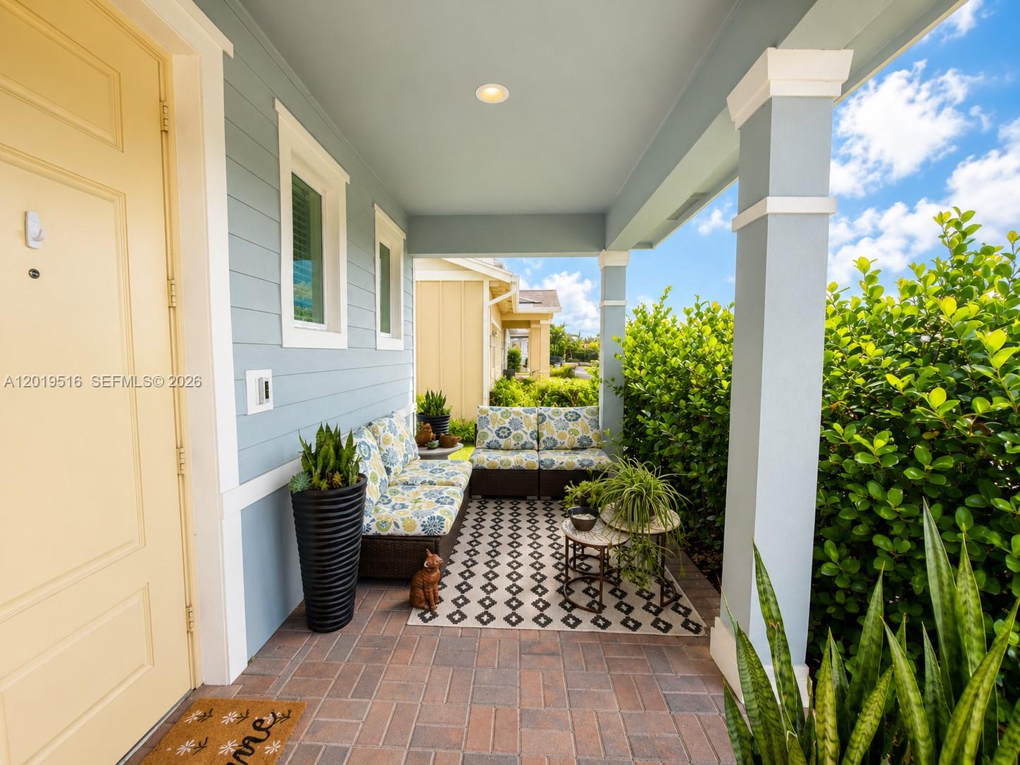 A covered porch features light blue siding, brick flooring, outdoor seating, and a patterned rug — 1248 Wandering Willow Way # 1248, Loxahatchee FL 33470, LOXAHATCHEE, FL