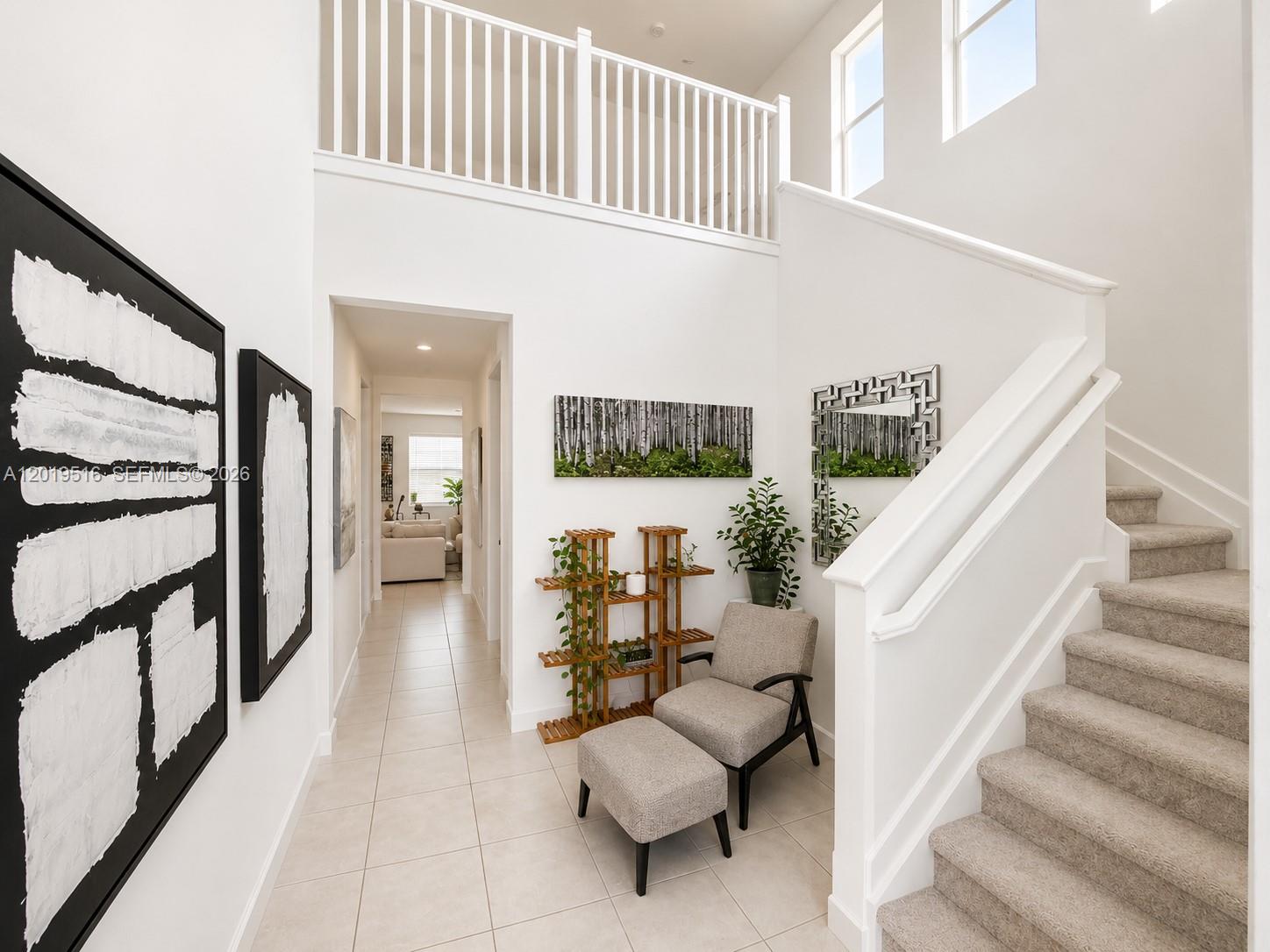 A bright entryway features a staircase, a reading chair with ottoman, and white tiled floors — 1248 Wandering Willow Way # 1248, Loxahatchee FL 33470, LOXAHATCHEE, FL