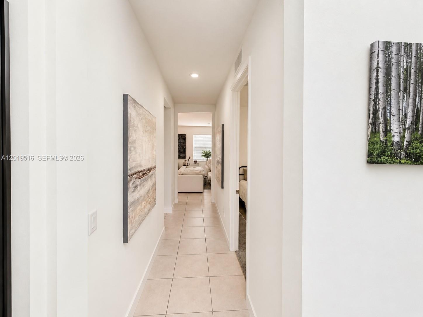 A tiled hallway leads to a living area, featuring white walls and two wall-mounted artworks — 1248 Wandering Willow Way # 1248, Loxahatchee FL 33470, LOXAHATCHEE, FL