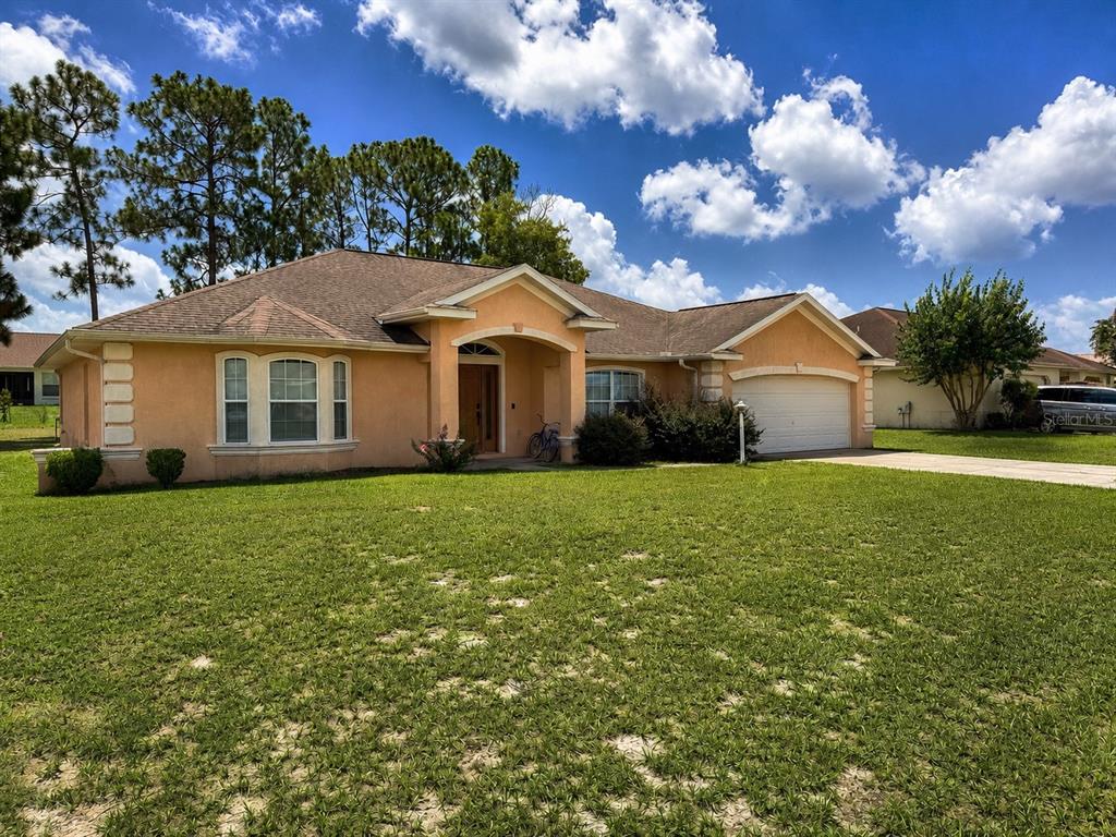 A single-story peach-colored house with a two-car garage and a large front lawn — 13405 SW 86TH AVENUE, OCALA, FL