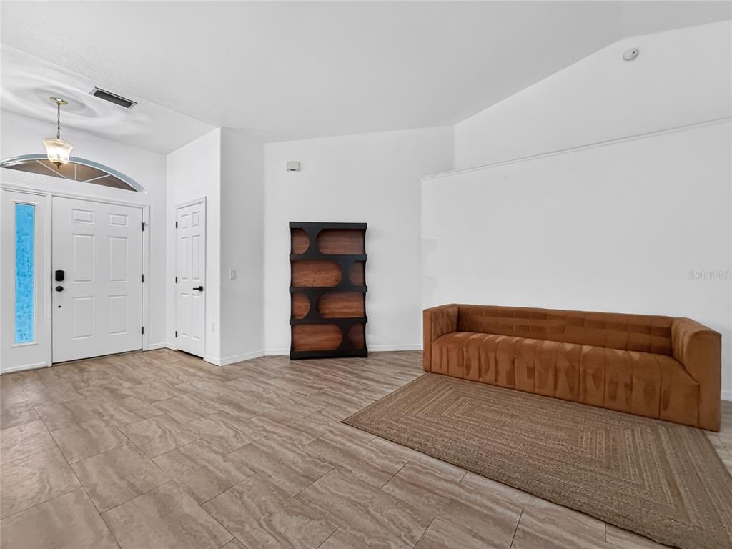 An entryway features a brown sofa on a rug, a tall bookshelf, and tiled floors — 13405 SW 86TH AVENUE, OCALA, FL