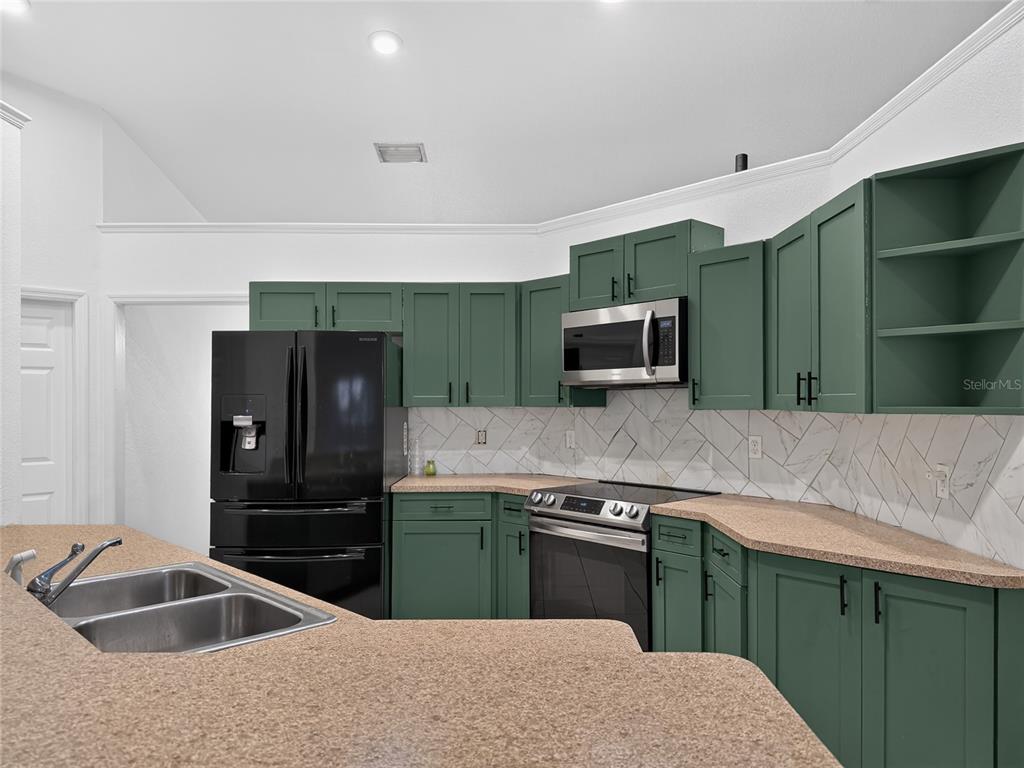 A kitchen features green cabinets, black appliances, a double sink, and a tiled backsplash — 13405 SW 86TH AVENUE, OCALA, FL