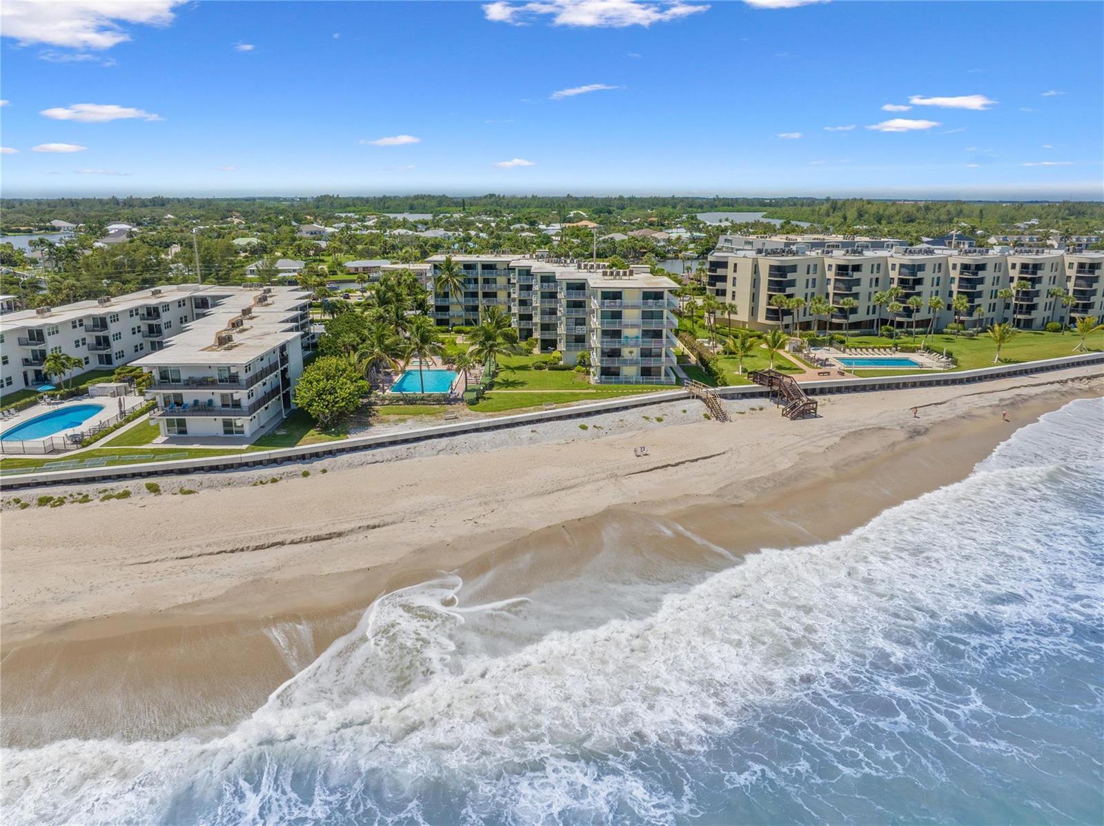 An aerial view shows three beachfront apartment buildings with swimming pools along a sandy shore — 4450 Highway A1a # 102, Vero Beach FL 32963, VERO BEACH, FL
