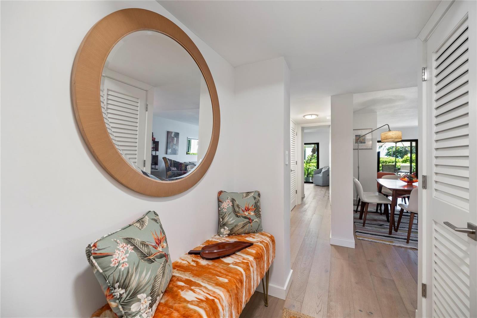A hallway features a round mirror, a patterned bench, and light wood flooring — 4450 Highway A1a # 102, Vero Beach FL 32963, VERO BEACH, FL