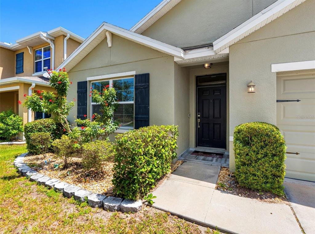 A tan house exterior features a black front door, a garage, and a landscaped yard — 8106 BILSTON VILLAGE LANE, GIBSONTON, FL