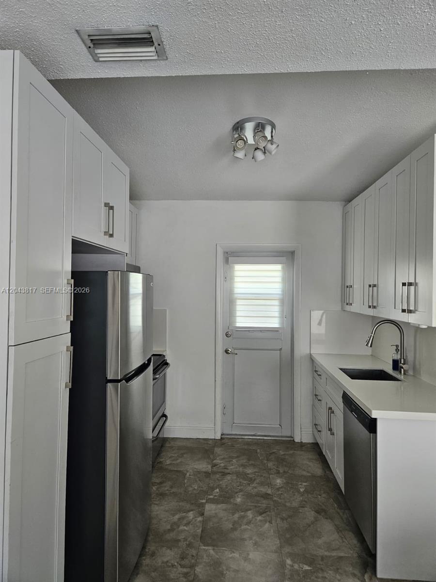 A galley kitchen features white cabinets, stainless steel appliances, and gray tiled flooring — 11000 SW 219th St, Miami FL 33170, MIAMI, FL