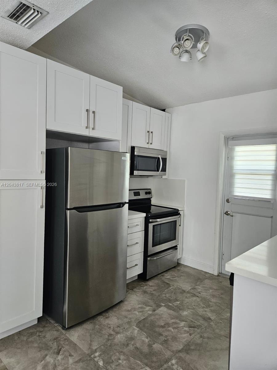 A kitchen features white cabinets, stainless steel appliances, and gray tile flooring — 11000 SW 219th St, Miami FL 33170, MIAMI, FL