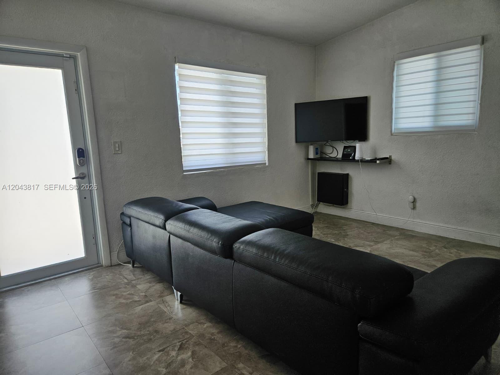 A living room features a black sectional sofa, tiled floors, and a wall-mounted television — 11000 SW 219th St, Miami FL 33170, MIAMI, FL