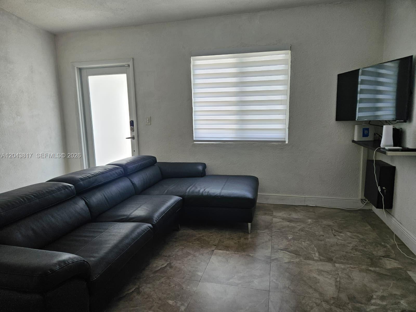 A living room features a black sectional sofa, tiled floors, a window, and a wall-mounted television — 11000 SW 219th St, Miami FL 33170, MIAMI, FL