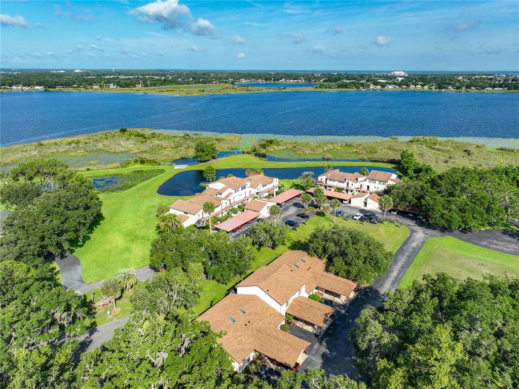 An aerial view shows multi-story residential buildings surrounded by trees, lawns, and a large lake — 4300 BAYWOOD BOULEVARD UNIT C106, MOUNT DORA, FL