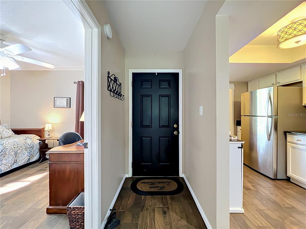 An entryway features a black front door, wood-look flooring, and adjacent views of a bedroom and kitchen — 4300 BAYWOOD BOULEVARD UNIT C106, MOUNT DORA, FL