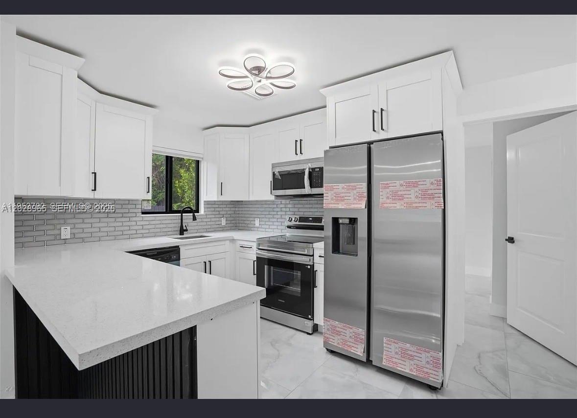 A modern kitchen features white cabinets, stainless steel appliances, a gray tile backsplash, and countertops — 1411 NW 40th St # 1, Miami FL 33142, MIAMI, FL