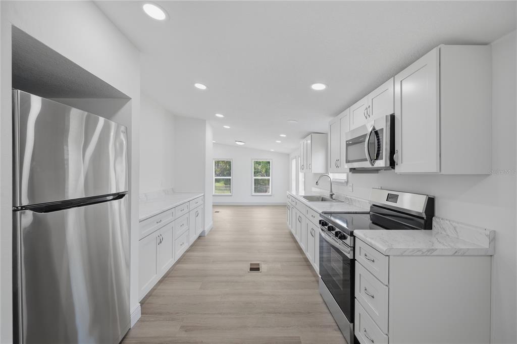A galley kitchen features white cabinets, stainless steel appliances, and light wood-look flooring — 7904 CADILLAC AVENUE, HUDSON, FL