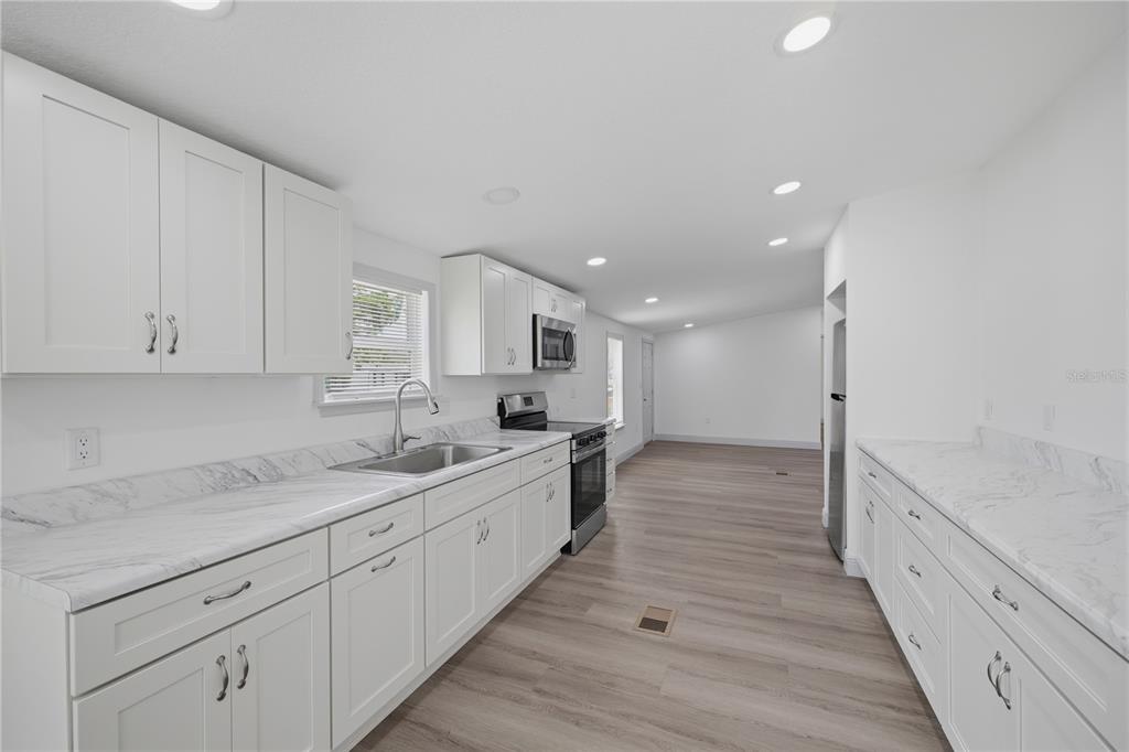 A kitchen features white cabinets, marble-look countertops, stainless steel appliances, and light wood-look flooring — 7904 CADILLAC AVENUE, HUDSON, FL